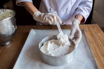Female chef cook in rubber gloves preparing vanilla cake-mix dough in form for baking cake. Young woman baker pouring the dough in baking dish