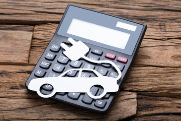 Paper Electric Car On Calculator At Wooden Table