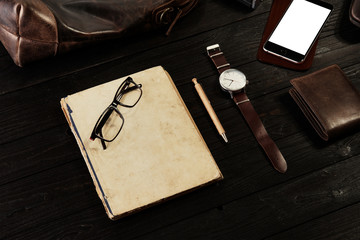 Mockup - Black phone with leather bag, old watch, glasses and book on dark wooden board