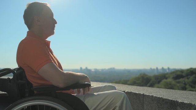 Pleasant concentrated wheelchaired man enjoying the city from observation point