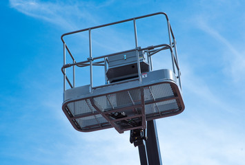 Hydraulic lift platform with bucket of yellow construction vehicle, heavy industry, blue sky and white clouds on background