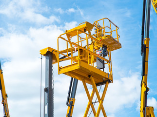 Hydraulic lift platform with bucket of yellow construction vehicle, heavy industry, blue sky and white clouds on background