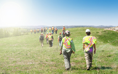 Group of workers in hardhats walking and inspecting grass field