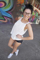 Sexy woman with jeans, shirt and glasses, posing in front of graffiti wall.