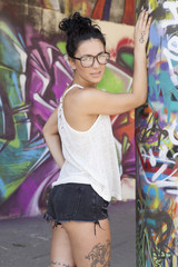 Fototapeta premium Sexy woman with jeans, shirt and glasses, posing in front of graffiti wall.