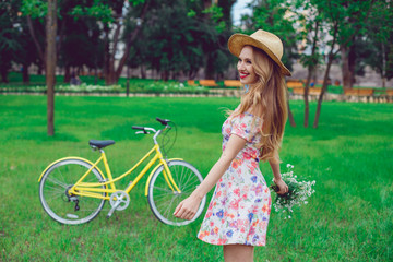 Beautiful happy young woman enjoying summer with wild-flower bunch. Happy girl dancing outdoor, relaxation and good mood in park, sunset. Bicycle on the background.