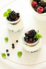 Healthy breakfast: yogurt with strawberry, blueberry and blackberry decorated mint leaves on white wooden table. Selective focus. Warm light