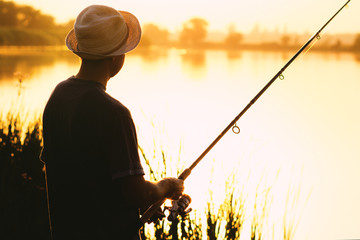 Silhouette of a man in a hat engaged in sport fishing