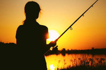 Silhouette of a fishing woman on the river bank at sunset
