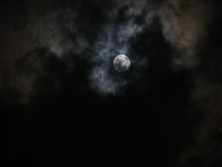 Naklejka na ściany i meble Photo of dark night full moon behind clouds, defocused background.