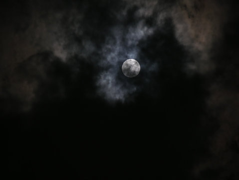 Photo of dark night full moon behind clouds, defocused background.