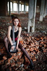 Red haired punk girl wear on black and red skirt, with bass guitar at abadoned place. Portrait of...