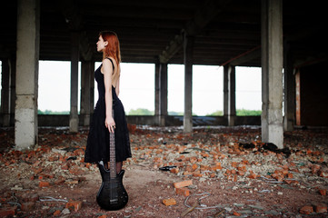 Red haired punk girl wear on black with bass guitar at abadoned place. Portrait of gothic woman...