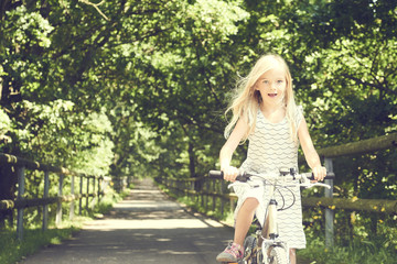 Fototapeta na wymiar Child blond girl riding a bicycle on a bike path in summer