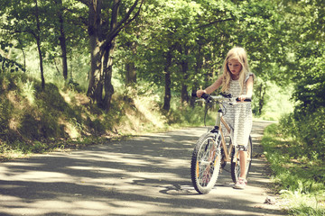 Obraz premium Child blond girl riding a bicycle on a bike path in summer