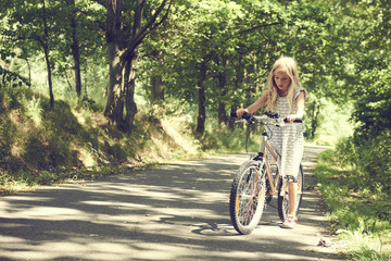 Child blond girl riding a bicycle on a bike path in summer