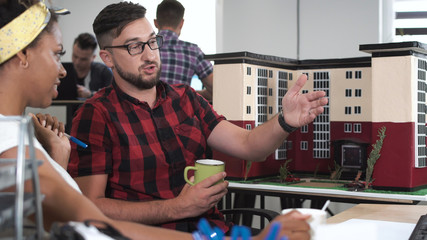 Man and woman sitting at table drinking cup of tea and working with mockup of building