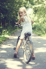 Naklejka premium Child blond girl riding a bicycle on a bike path in summer