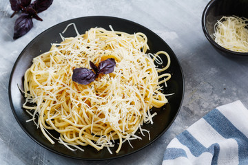 Black plate with Italian spaghetti with basil and parmesan on a gray table