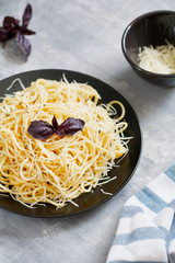 Black plate with Italian spaghetti with basil and parmesan on a gray table