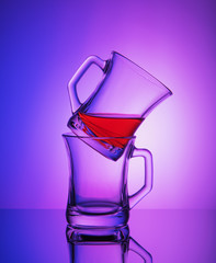 Close view of two empty crystal cups with the rest of tea on the gradient blue and purple background. Reflective surface.