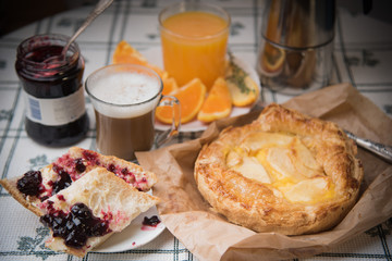 A cozy sweet breakfast in bright colors. Apple pie with cherry jam and cups of fresh hot coffee and orange juice.