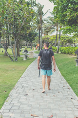Fototapeta na wymiar Rear view of man with backpack walking in the beach park of Nusa Dua, Bali island, Indonesia.
