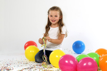 Kind sitzt mit Luftschlange zwischen Luftballons