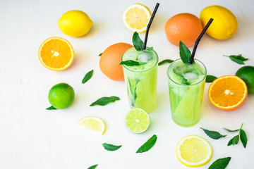 Tasty transparent refreshing drink with cucumber, limes and orange on white wooden table