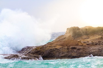 Fototapeta na wymiar The waves breaking on a stony rock, forming a spray.