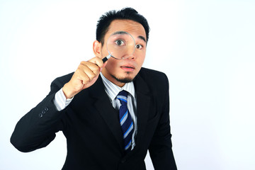 Asian Businessman looking through a magnifying glass isolated on white.jpg