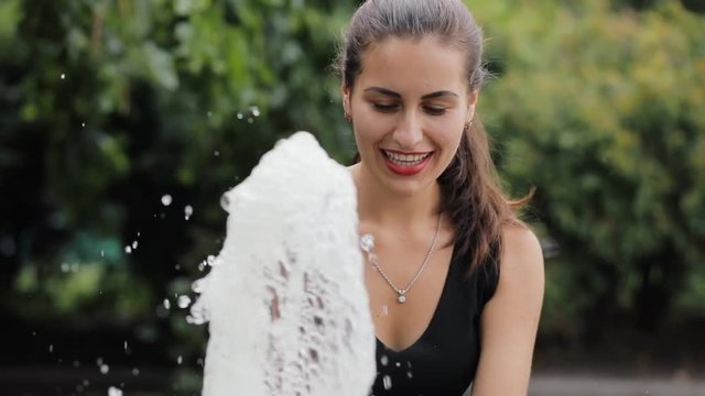 Pretty woman wash up her face from fountain in slowmotion. Freshness water in a warm summer day.