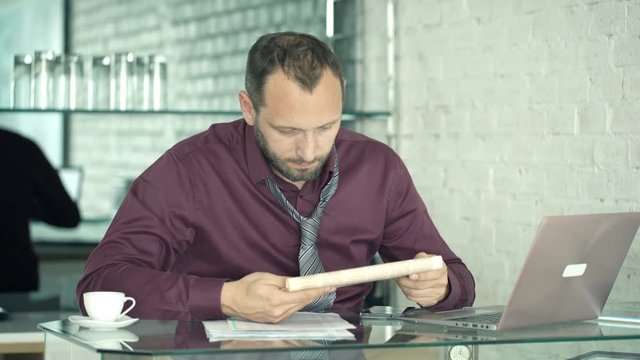 Young businessman reading newspaper sitting by table in kitchen at home
