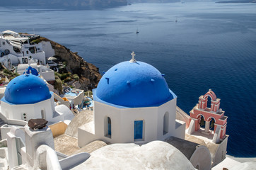 Oia Village, Santorini Cyclade islands, Greece. Beautiful view of a blue dome church and a pink tower-bell.