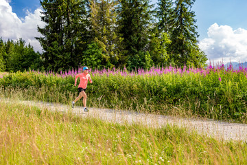 Young woman running on country road in mountains, summer day