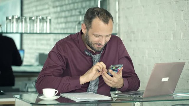 Young businessman texting on smartphone sitting by table at home
