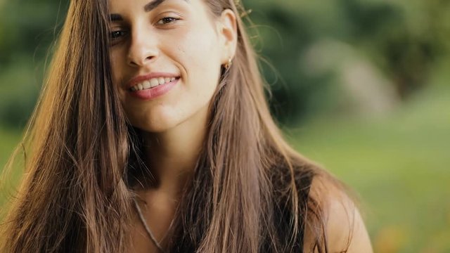 Closeup portrait of pretty modest woman with beautiful hair in a park at summer day