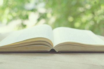 Blurred image of the open book in front of an open window with green trees. The concept of...