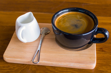Dark black blue coffee cup with americano coffee, spoon and a milk jug on a wooden stand