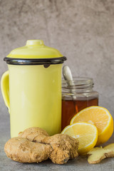 
 Prevention and treatment of influenza and colds. The root of ginger, fresh lemon, a glass jar with honey and a high mug with hot tea on a gray background. Used in folk medicine.