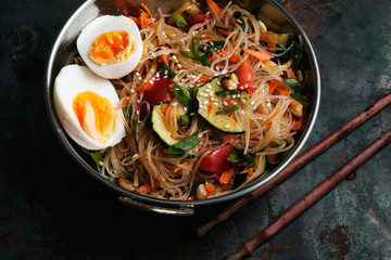Spicy veggie wok: rice noodles with zucchini, onion and sesame. Asian styled lunch on metal textured background. Horizontal composition with copy space for text