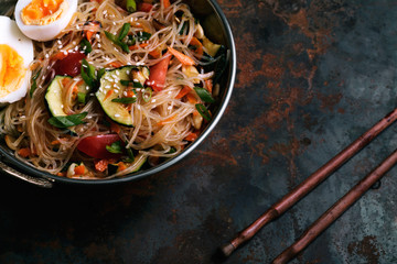 Spicy veggie wok: rice noodles with zucchini, onion and sesame. Asian styled lunch on metal textured background. Horizontal composition with copy space for text