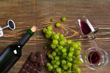 Red wine bottle, grape, cheese and glasses over wooden table. Top view with copy space