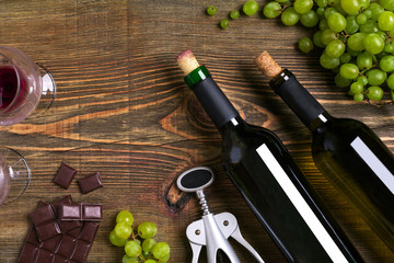 Red and white wine bottles, grape, chocolate and glasses over wooden table. Top view with copy space