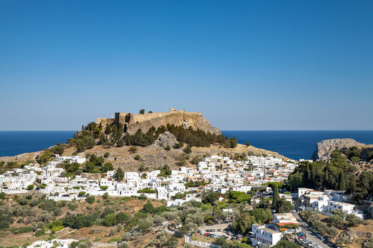 Lindos town at the foot of the mountain. Acropolis of Lindos is located on a hill above the town. Bay and harbor with beach.