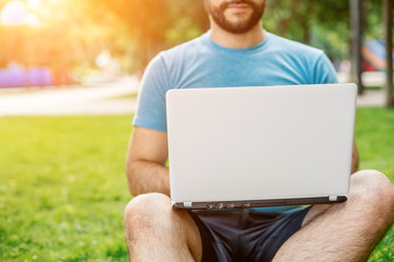 Young man using and typing laptop computer in summer grass.