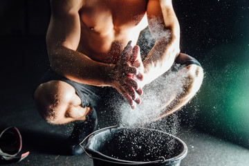 Fitness model trainer rubs his hands with chalk and talc so that fingers do not slip or slide. - Powered by Adobe