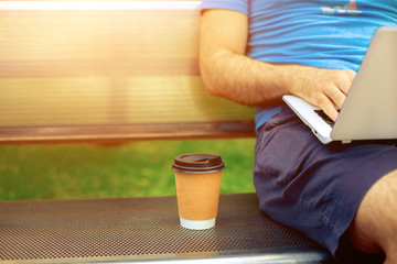 Casual dressed man sitting at wooden beanch inside garden working on computer.
