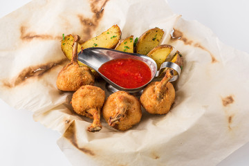 Fried chicken legs breaded and potato with sauce on a sheet of parchment