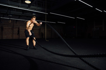 Fitness man workout with battle ropes at gym. training exercise fitted body in club. Torso.